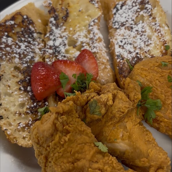 Plate of powdered-sugar French toast with strawberries and crispy fried chicken garnished with parsley.