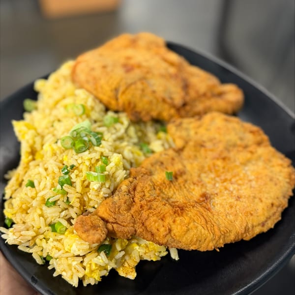 Black plate of fried chicken tenders with scallion-topped fried rice.