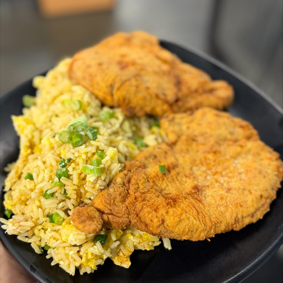 Black plate of fried chicken tenders with scallion-topped fried rice.