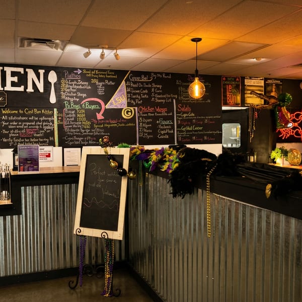 A vibrant restaurant interior with a chalkboard menu, Mardi Gras decorations, and a bar area.