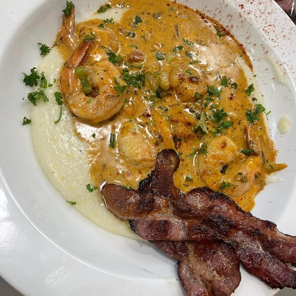 Creamy shrimp and bacon served over grits, garnished with chopped parsley and vegetables on a white plate.