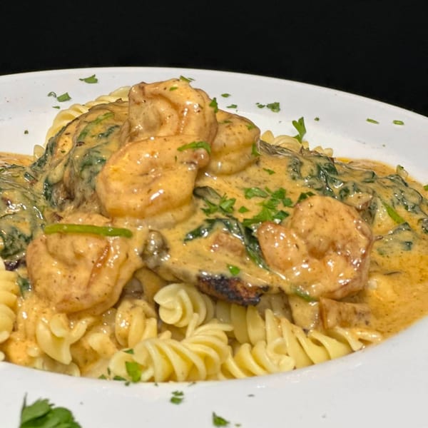 Creamy chicken and mushroom pasta with spinach, spiral noodles, and chopped parsley on a white plate.