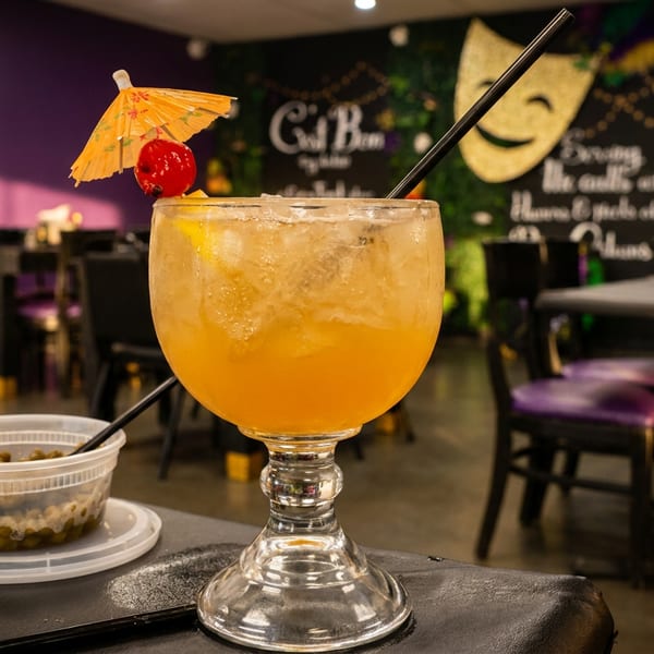 A large orange cocktail with a tiny umbrella and cherry, next to a container of olives.