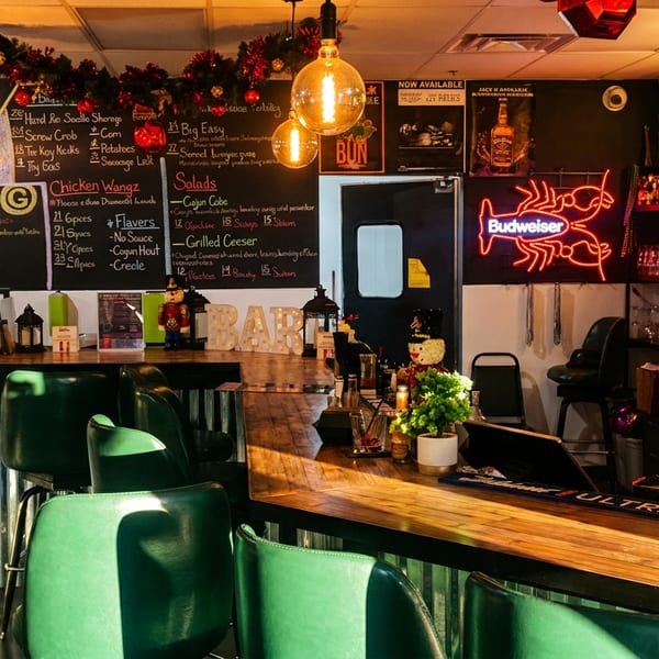 A vibrant bar interior with green stools, a wooden counter, neon signs, and a chalkboard menu.